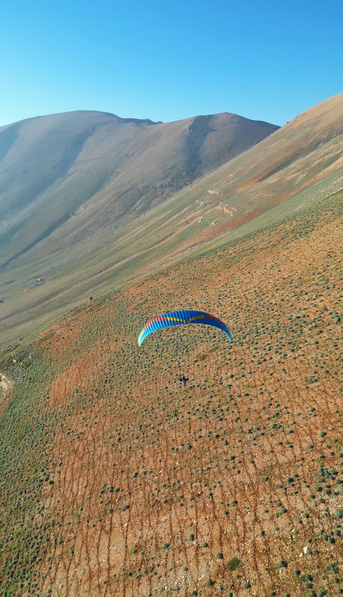 Colorful paraglider over arid Cedars highland mountains under blue sky