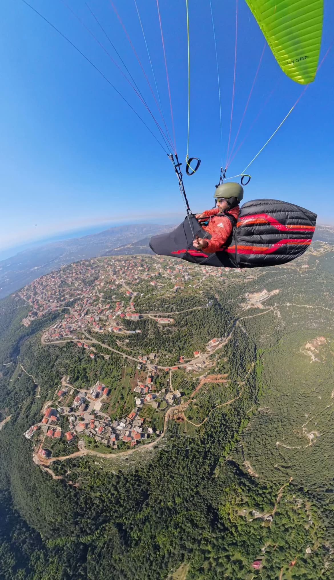 Paraglider above green Miziara mountain ridge and terracotta village roofs